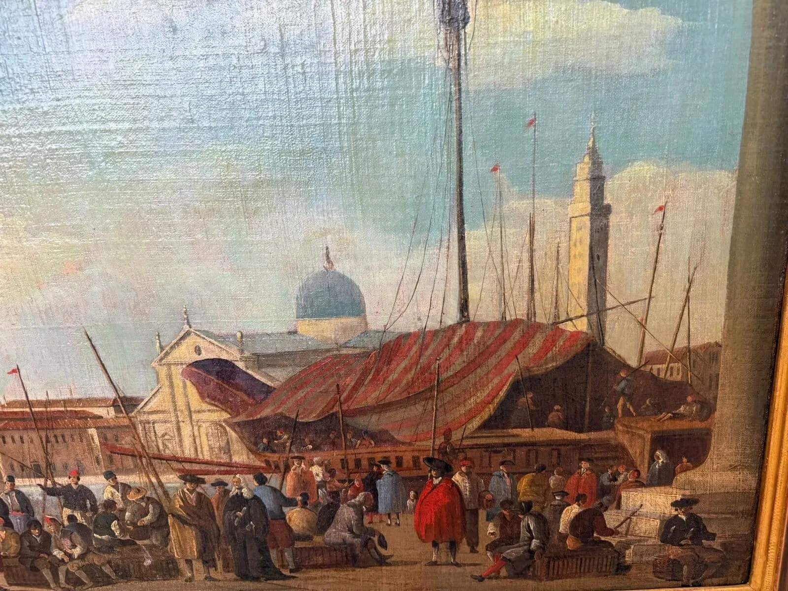 Une scène animée du port de Neuchâtel, avec de nombreuses personnes rassemblées près des bateaux. Un grand auvent rayé recouvre une partie d'un navire. À l'arrière-plan, des bâtiments avec des dômes et de hautes tours s'élèvent sous un ciel bleu nuageux.