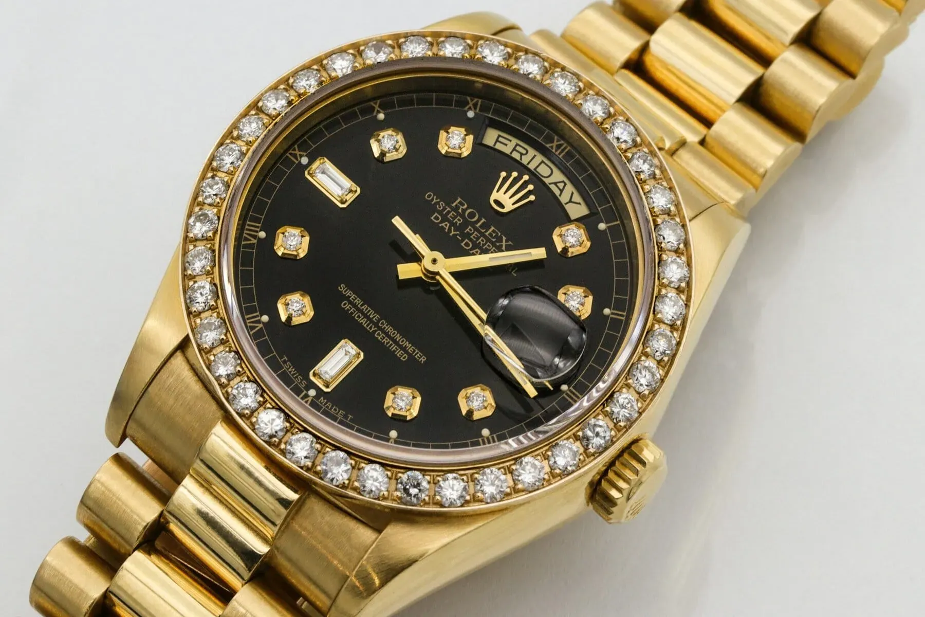 Montre-bracelet Rolex en or avec cadran noir, index en diamants, lunette incrustée de diamants et affichage de la date et du jour, présentée sur un bracelet à maillons en or - une icône de la légende horlogère - sur un fond blanc.
