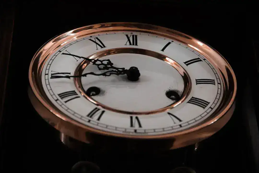 Gros plan sur une horloge vintage avec un cadran blanc, des chiffres romains noirs et des aiguilles ornées. L'heure indique 9:15. Cette pièce d'horlogerie française du XVIIIᵉ siècle présente un bord en or poli et une usure visible près des trous de remontage.
