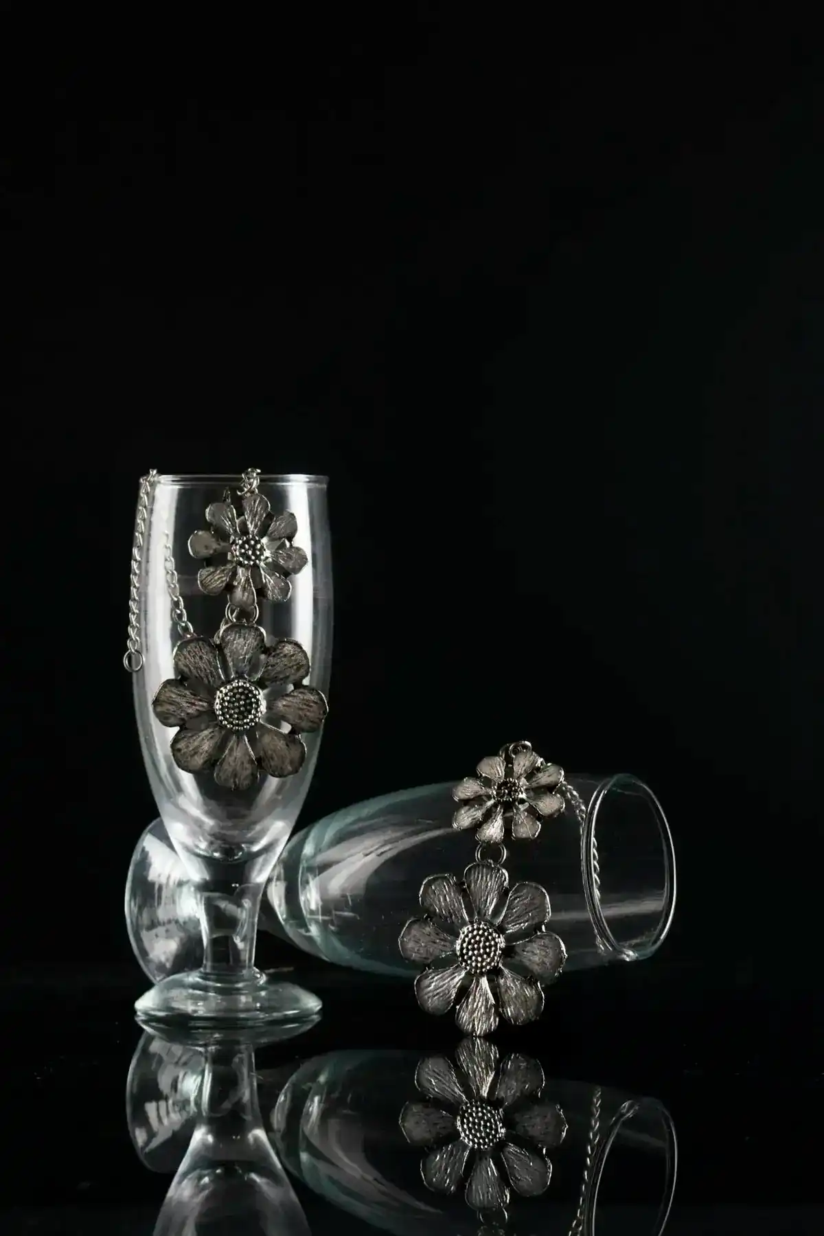 Silver floral jewelry artistically displayed in clear glasses against a black backdrop.