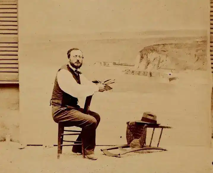 Homme peignant un paysage côtier assis sur une chaise