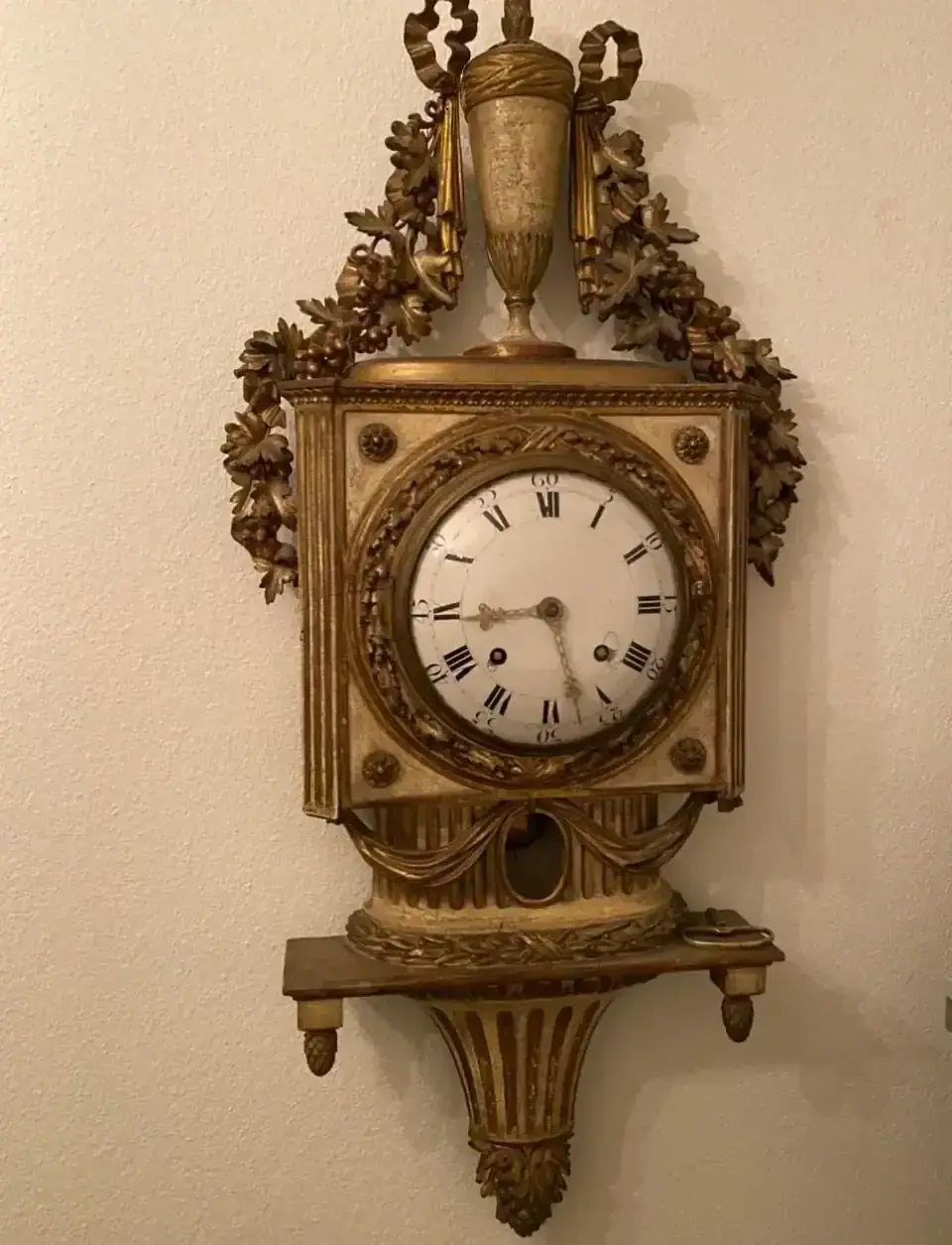 Ancienne horloge murale dorée avec chiffres romains.