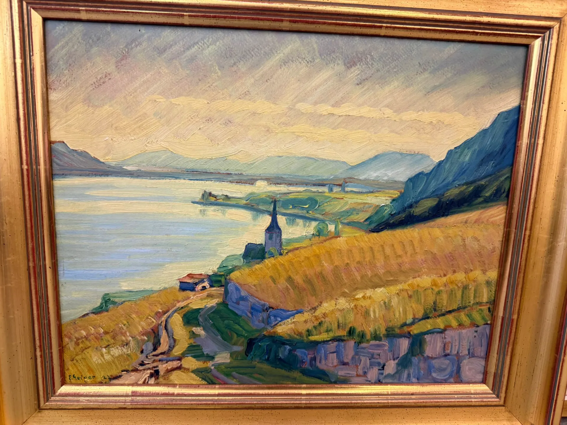 Peinture encadrée d'un paysage lacustre avec des vignobles en terrasses, un chemin sinueux et une église avec un haut clocher à côté d'un vieux colombier. Les montagnes et l'eau bleue s'étendent au loin sous un ciel légèrement nuageux. Les coups de pinceau sont vifs et visibles.